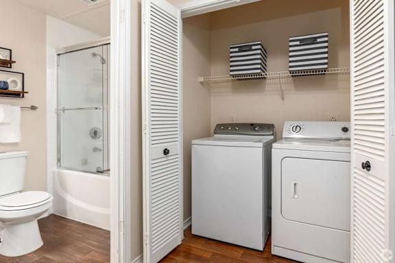 A white toilet is in a bathroom next to a white cabinet and a white dryer.