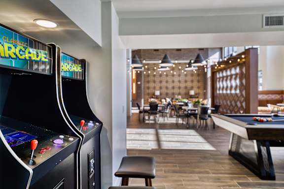 A black arcade machine sits next to a pool table in a room with a wooden floor.