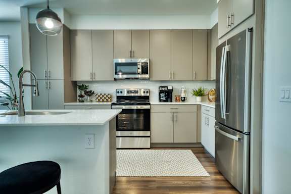 A modern kitchen with a stainless steel refrigerator and a black bar stool.