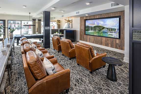 A large screen TV mounted on a wooden wall in a room with leather chairs.