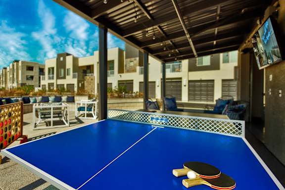 A blue ping pong table with two paddles on it. at Craft at Gilbert and Baseline Apartments, Mesa, AZ, 85204