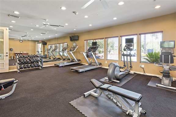 A spacious gym with a variety of equipment including treadmills, weight machines, and a bench press at Superstition Canyon Apartments, Mesa, AZ, 85209