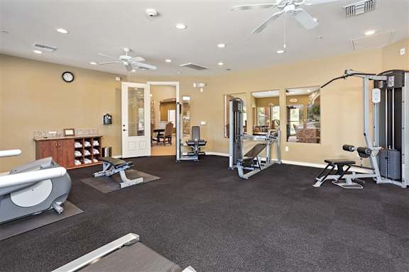 A spacious gym with a variety of equipment including a treadmill, weights, and a bench press at Superstition Canyon Apartments, Mesa, 85209