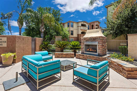 Two lounge chairs are placed on a patio in front of a fireplace. at Superstition Canyon Apartments, Mesa, Arizona