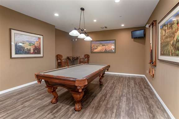 A pool table in a room with brown walls and wooden flooring. at Superstition Canyon Apartments, Mesa