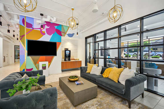 A modern living room with a grey sofa and a colorful abstract wall art. at Link Apartments® 4th Street, Winston-Salem, North Carolina
