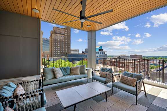 A patio with a couch, chairs, and a table with a view of the city. at Link Apartments® 4th Street, Winston-Salem, North Carolina