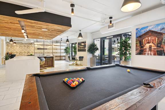 A pool table is in the middle of a room with a ceiling fan and a painting on the wall. at Link Apartments® 4th Street, Winston-Salem, North Carolina
