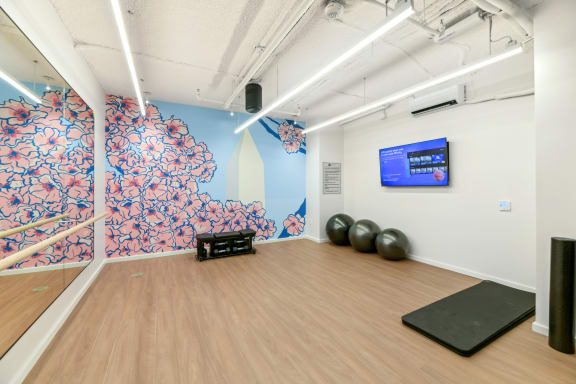 a yoga studio with a wooden floor and a wall with a screen and exercise balls  at Link Apartments® H Street, Washington