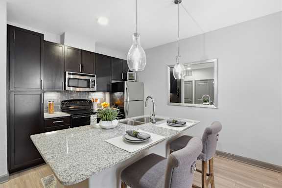 A modern kitchen with a granite countertop and dark brown cabinets.