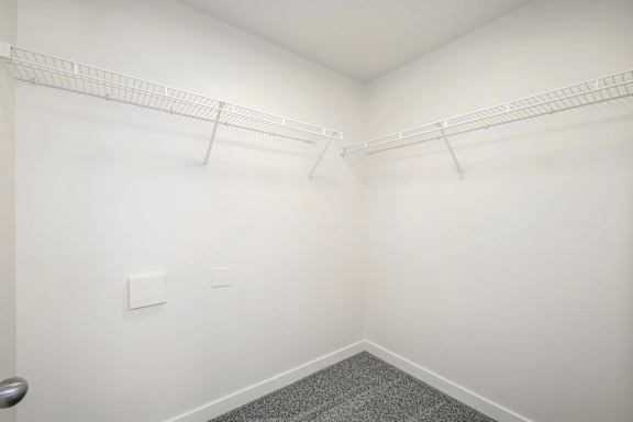 A white closet with a grey carpet and two white shelves.