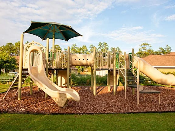 A playground with a green umbrella and two slides.