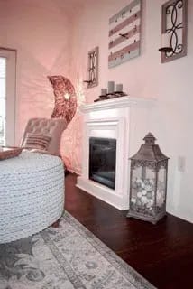 A white fireplace with a lantern on the floor.
