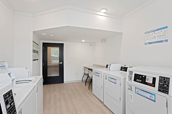 A laundry room with a washer and dryer on the right and a black door in the middle.
