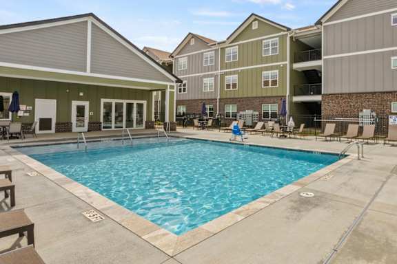 A large swimming pool in front of a building with a patio area.
