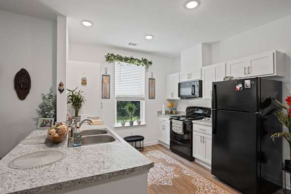 A black refrigerator is in a white kitchen with a sink and a window.
