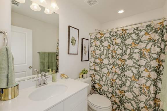 Bathroom with botanical print shower curtain and white vanity at The Courts at Maverick Yards Apartments, Mauldin, SC
