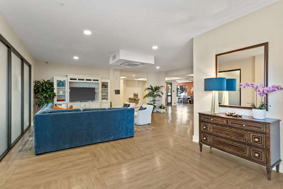A blue couch sits in a spacious living room with a wooden floor and a large mirror on the wall.