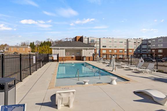 A pool surrounded by chairs and a fence.