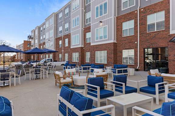 A patio with blue chairs and tables in front of a brick building.