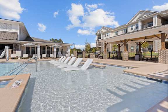 A large outdoor swimming pool with sun loungers and a building in the background.