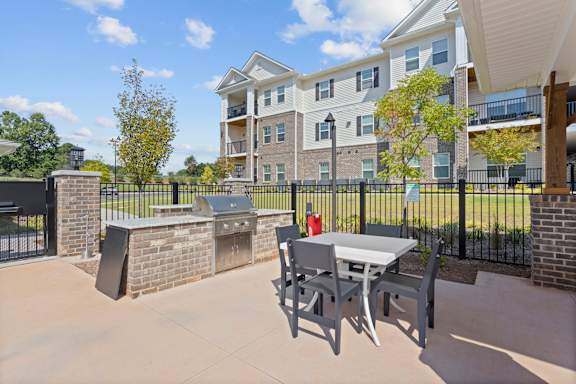 A patio with a table and chairs is in front of a brick wall and apartment building.