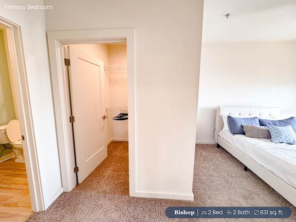 A bedroom with a bed, a chair, and a doorway leading to another room.