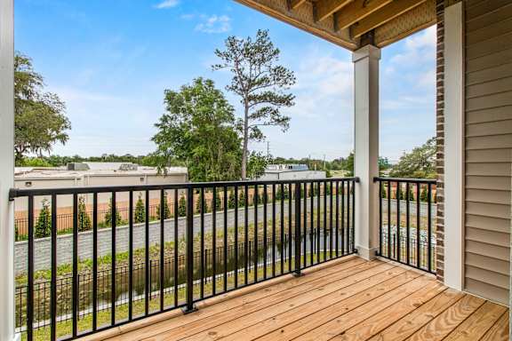 A wooden deck with a black railing and a view of a street and trees.