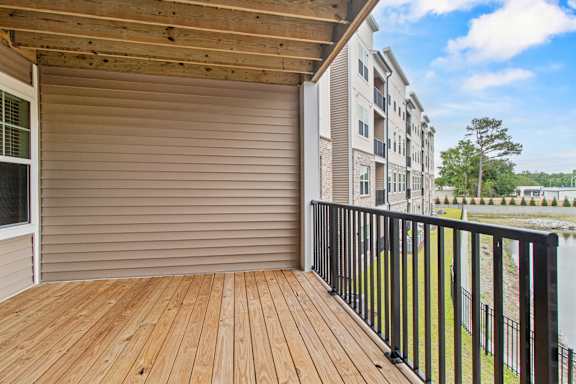 A wooden deck with a black railing and a sliding glass door leading to a balcony.