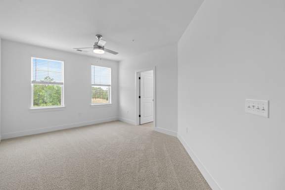 A room with a carpet floor, a ceiling fan, and a door.