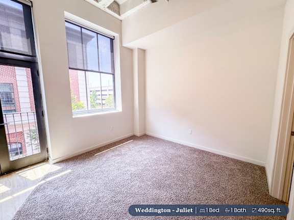 A bedroom with a large window and a carpeted floor.