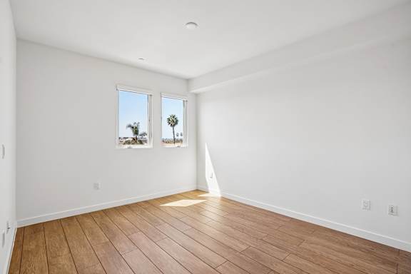 A room with wooden flooring and two windows.