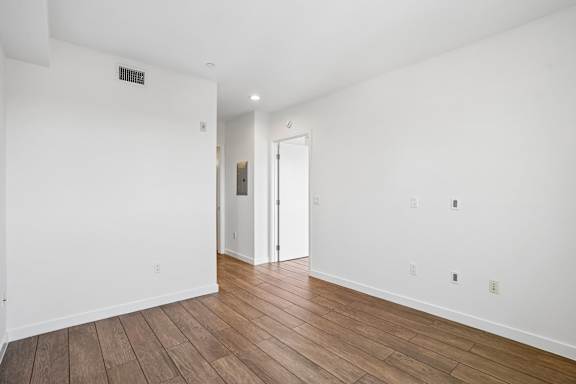 A room with white walls and wooden flooring with a doorway leading to another room.