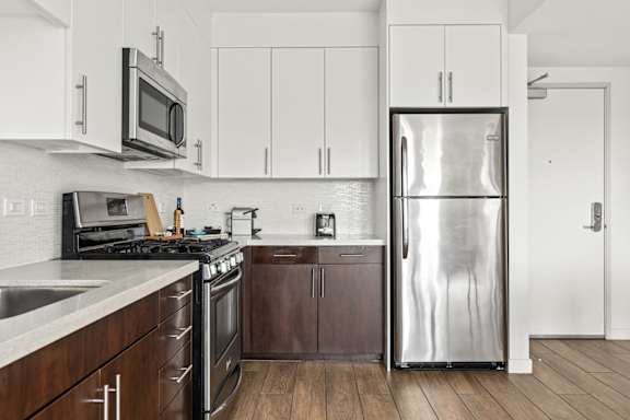 A modern kitchen with a stainless steel refrigerator, microwave, and oven. With cabinets.
