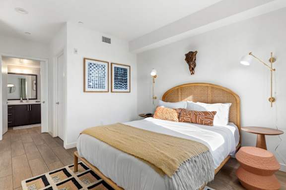 Bedroom with a bed, a table, a rug, lamps and paintings on the wall.