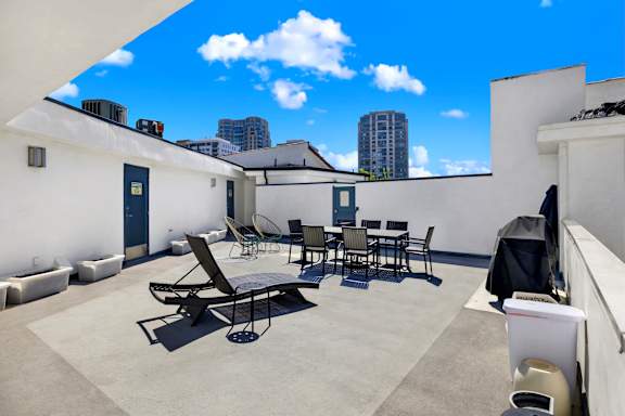Rooftop patio with chairs, a table, and bbq is shown with a blue sky in the background. at The Hilgard, Los Angeles, CA
