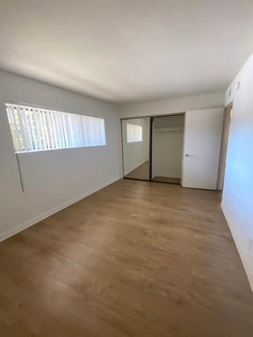 A room with wooden flooring and a window with blinds.