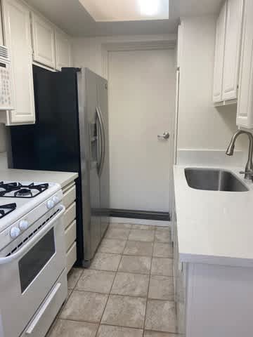 A kitchen with a black refrigerator, white cabinets, a stove, and a sink.