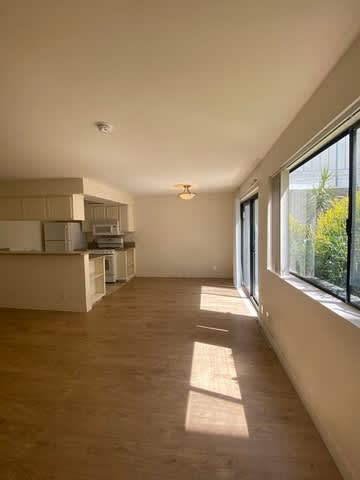 A spacious room with a kitchen area and wooden flooring.