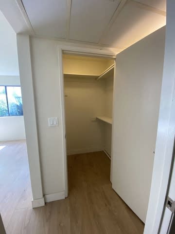 A white door is open to a small room with wood flooring.