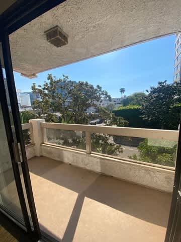 A balcony with a glass door overlooks a tree-filled street.