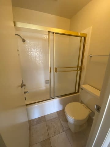 A white toilet sits in a bathroom with a gold framed shower door.