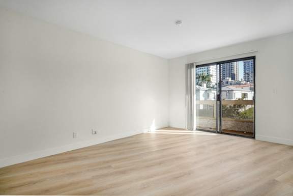 Empty room with wooden floor and sliding glass door.