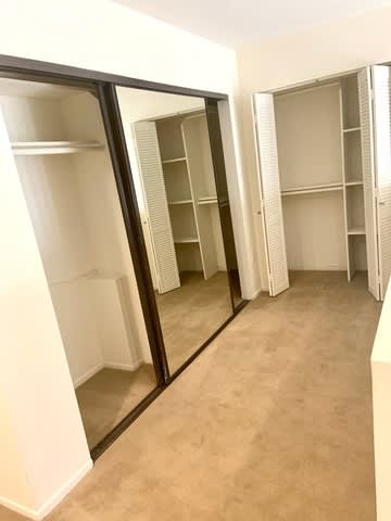 A room with a mirrored closet door and empty shelves.