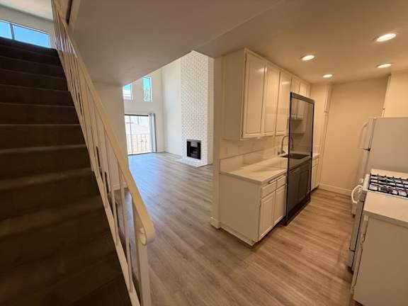 A kitchen with white cabinets and a staircase on the left side.