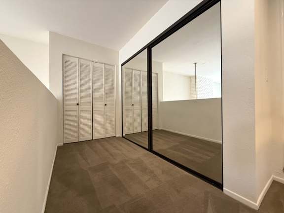 A hallway with a mirrored wall and a row of closets.