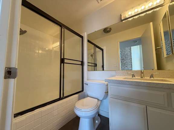 A white toilet sits in a bathroom with a sink and mirror.