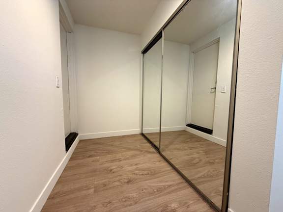 A hallway with a mirror on the wall and wooden flooring.