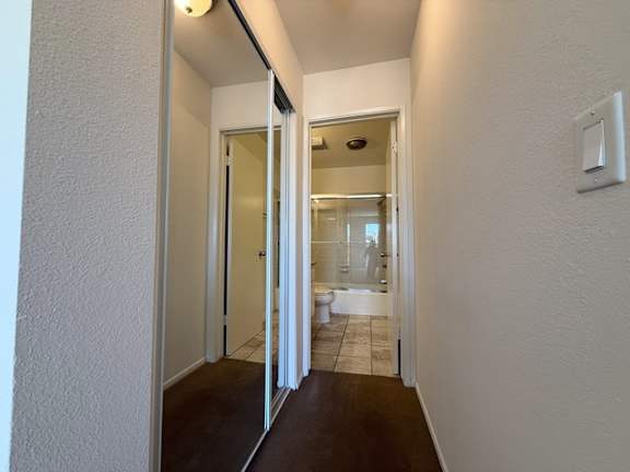 A hallway with a toilet and sink visible through the door.
