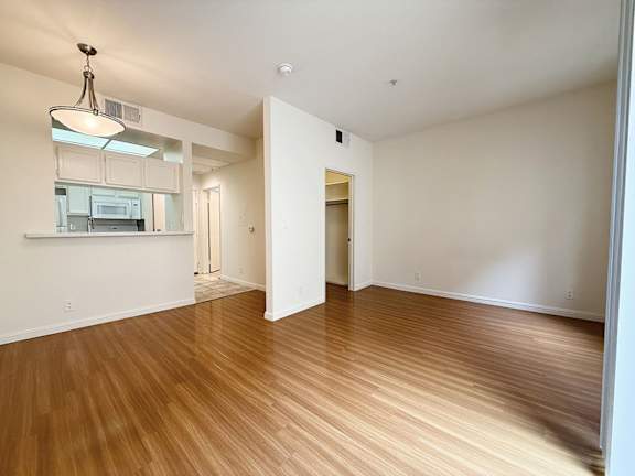 A room with wooden floors and a kitchen area in the background.